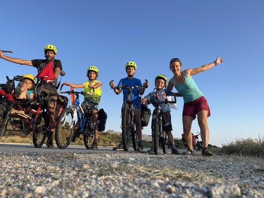 Delphine, Yann et leurs quatre enfants posent avec leurs vélos chargés de sacoches, sur une route au soleil couchant.
