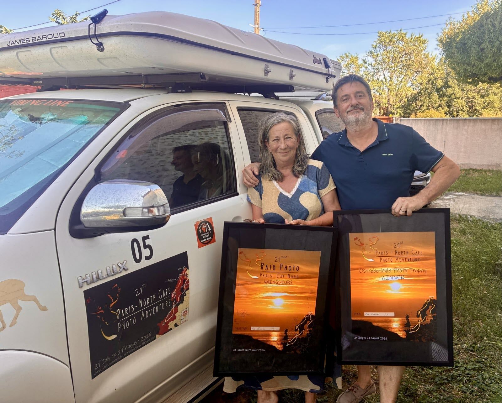 Pascale et François devant leur 4×4 de rallye, tenant chacun un trophée photo encadré.