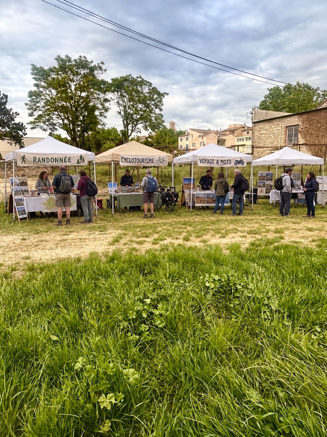 Des stands sous barnums blancs dans un pré, avec des visiteurs qui discutent.