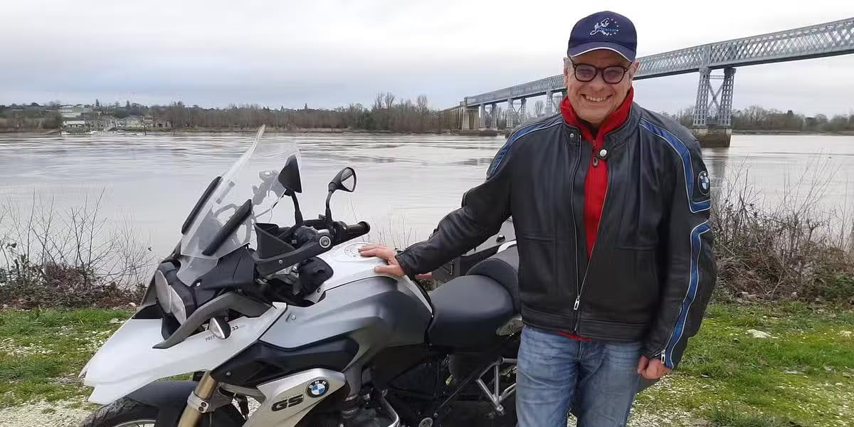 Yannick Grimaud, casquette et veste de moto, à côté de sa moto au bord d'un fleuve.